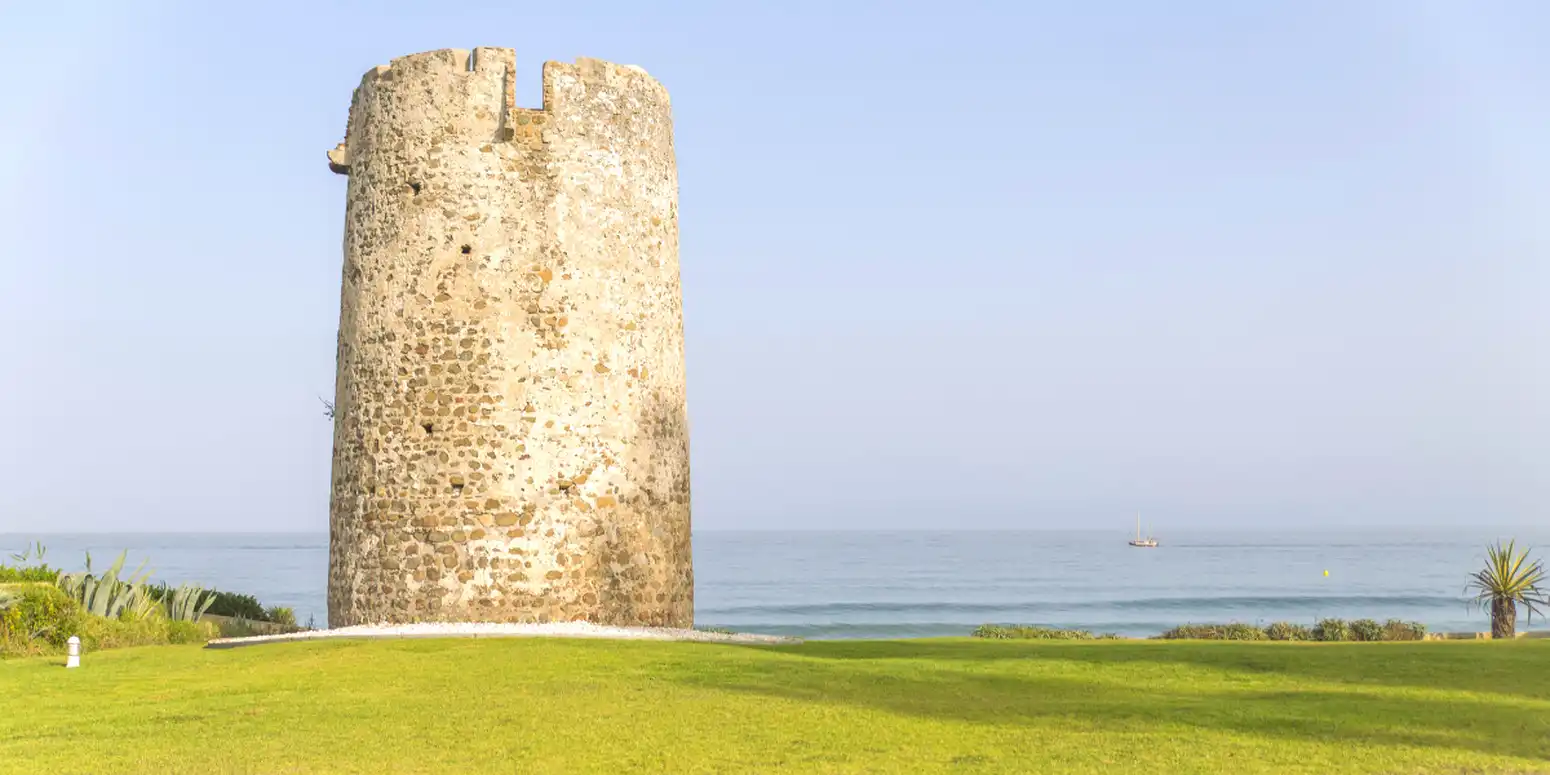 Old coastal watchtower by the sea with grassy foreground and Mediterranean views